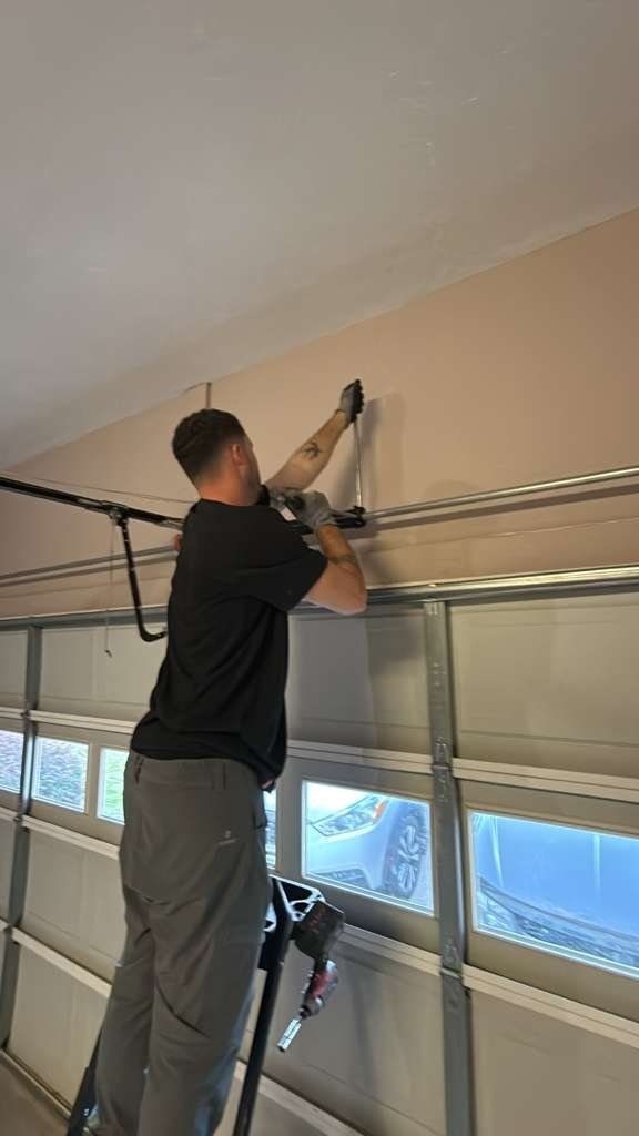 Technician standing on a ladder at the top edge of a garage door