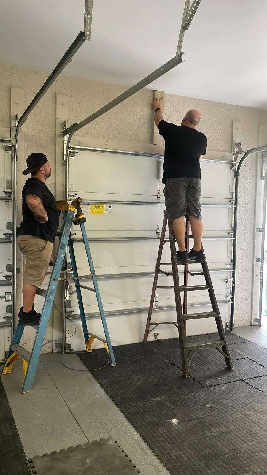 Technician on a stepladder at the door header with a helper on the left