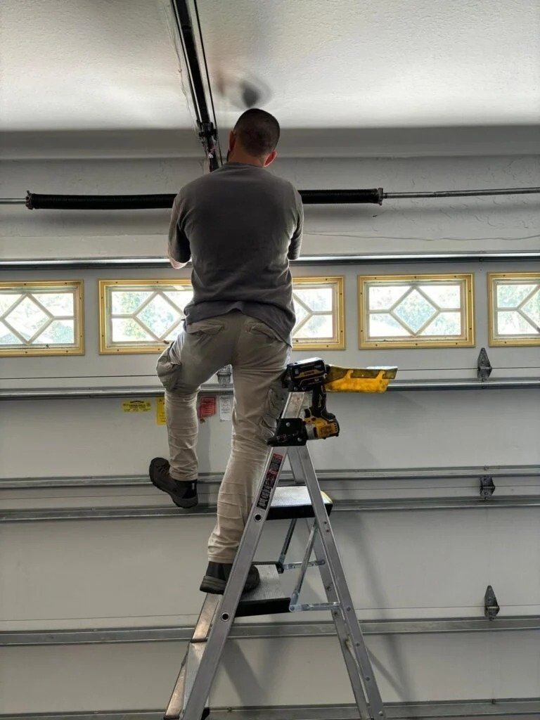 Technician on a stepladder working above a garage door with a row of small windows