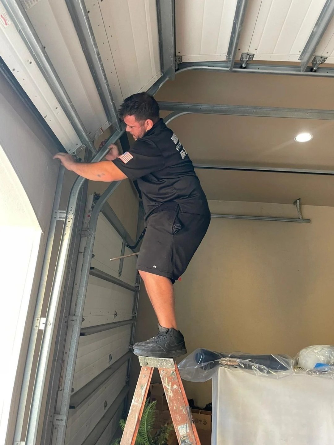 Technician standing on a stepladder and reaching the upper track corner of a garage door