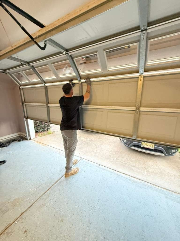 Garage door hanging crooked in its track while a person steadies one side