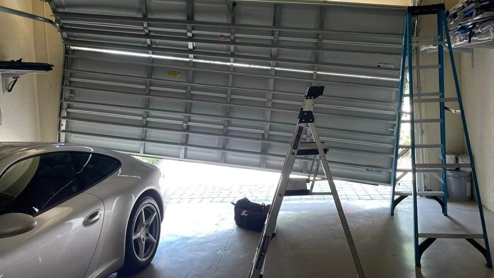 Stepladder set up under a raised steel garage door beside a parked car
