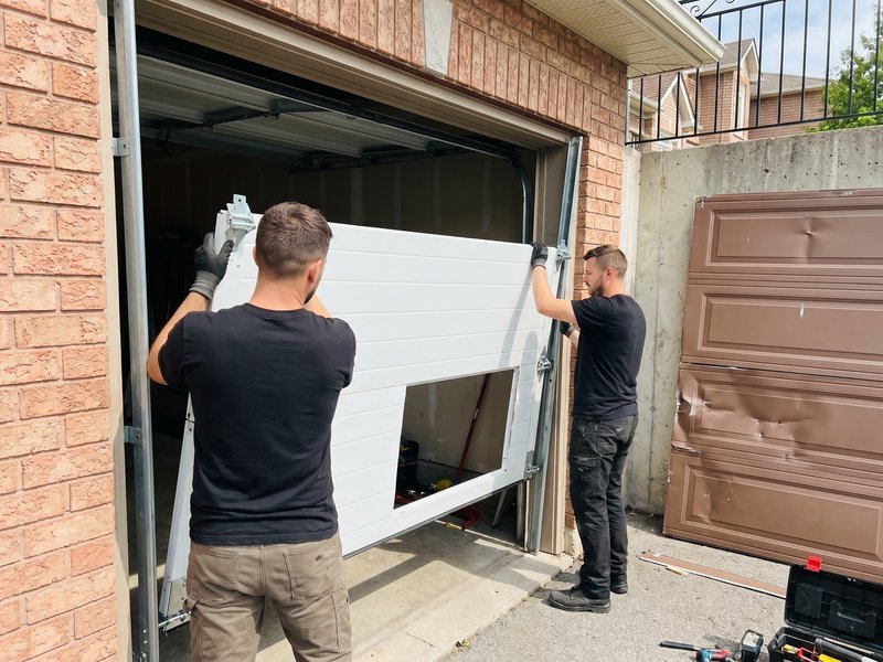 Two installers lifting a new panel into a brick-framed garage