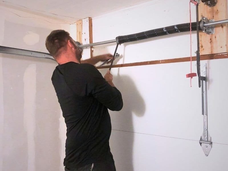 Technician working on a torsion spring above a white garage door